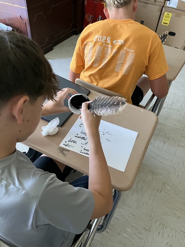 8th grade students using a feather pen they made to practice signing their name