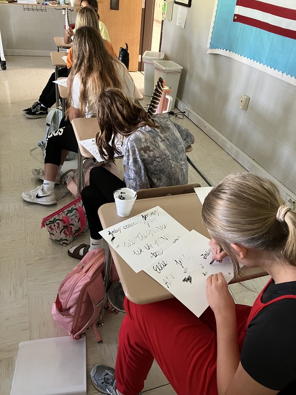 8th grade students practice writing name with feather pens