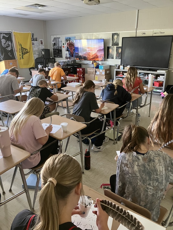 8th grade students practice writing name with feather pens