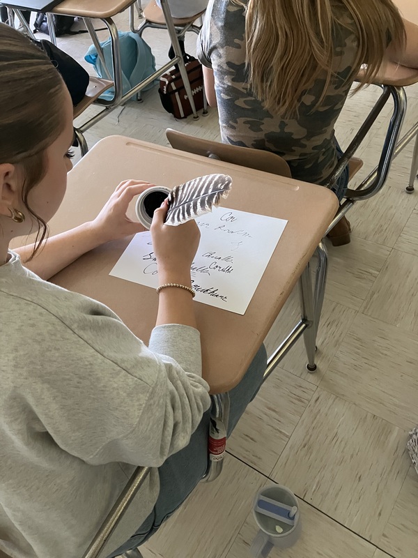 8th grade students practice writing name with feather pens