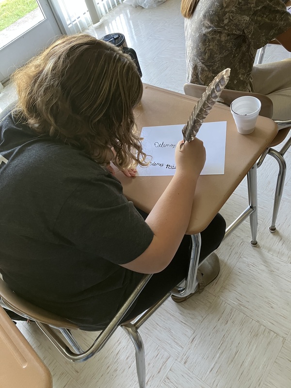 8th grade students practice writing name with feather pens