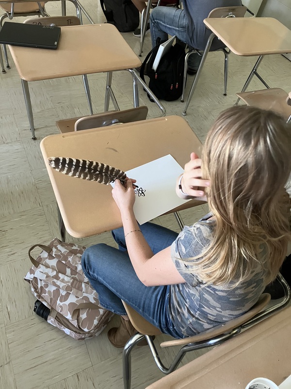 8th grade students practice writing name with feather pens