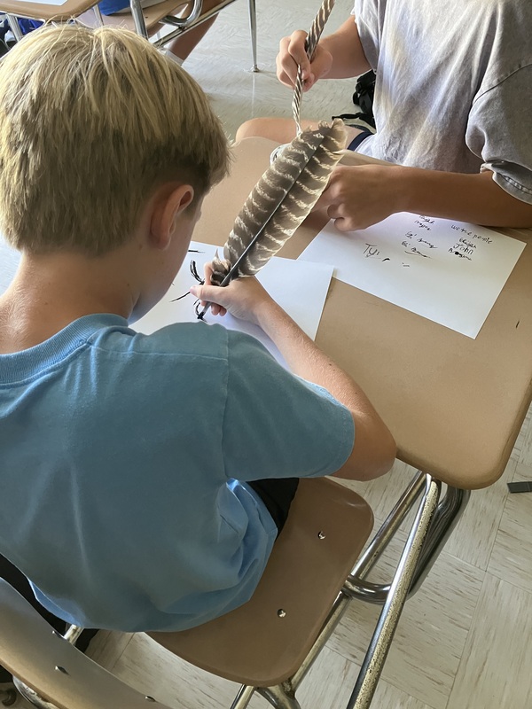 8th grade students practice writing name with feather pens