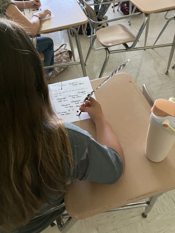 8th grade students practice writing name with feather pens
