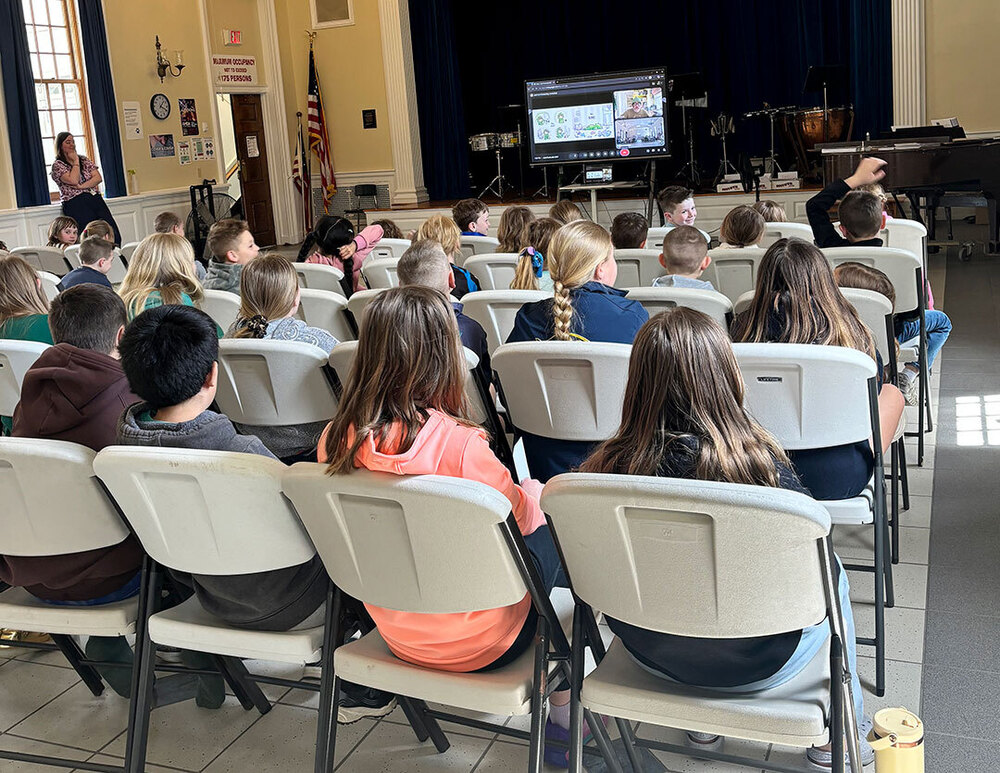 students seated in auditorium watch virtual visit with author who appears on screen at the front of the room