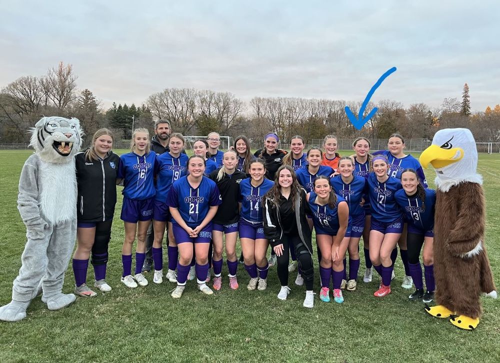 girls varsity soccer team stands with mascots on soccer field