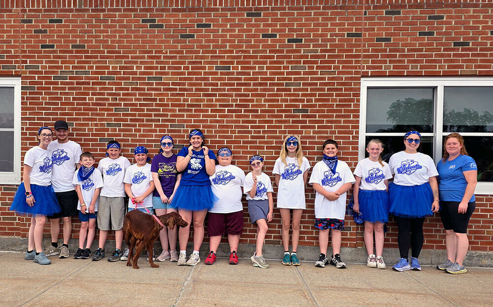 ODY On the Run Team and coaches stand together in front of a brick school building