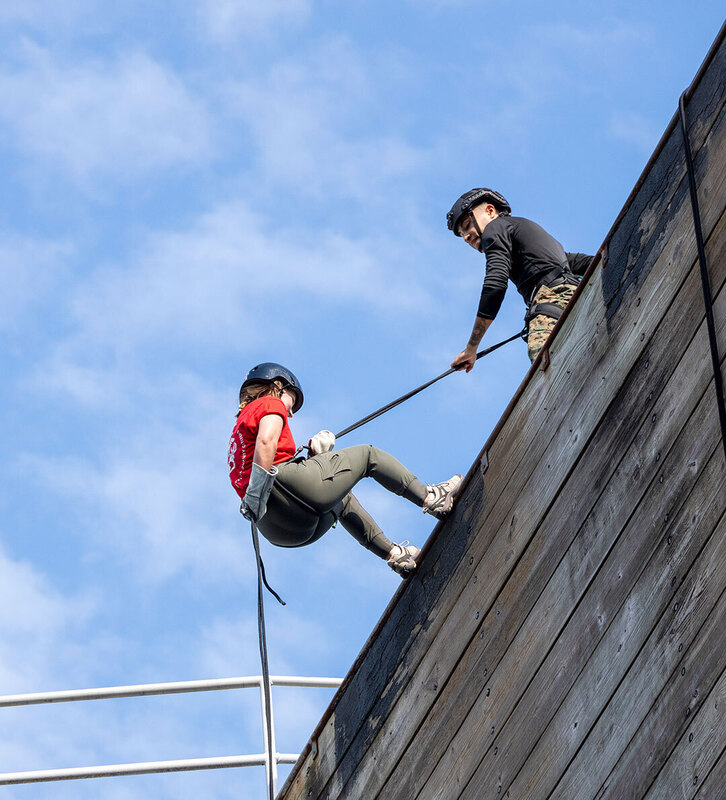 teacher wearing helmut and holding ropes repels down 60 foot wall 