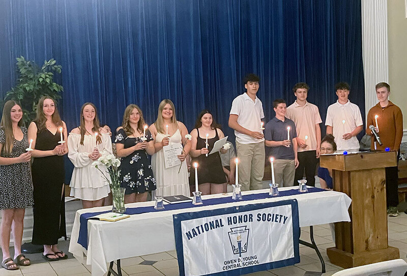 Students stand on stage holding candles at the National Honor Society induction ceremony