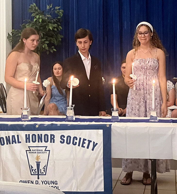 Three students light candles representing the pillars of the National Honor Society