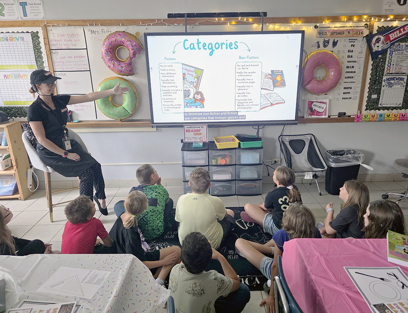 A teacher presents different categories of books on a white board to the fourth-grade class