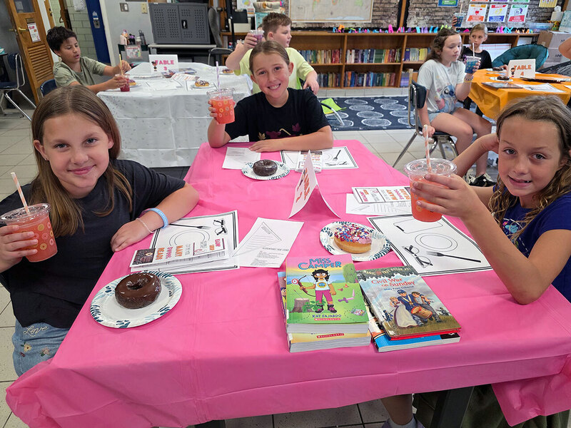 Three students sit at desks with reading materials while enjoying Dunkin donuts and drinks
