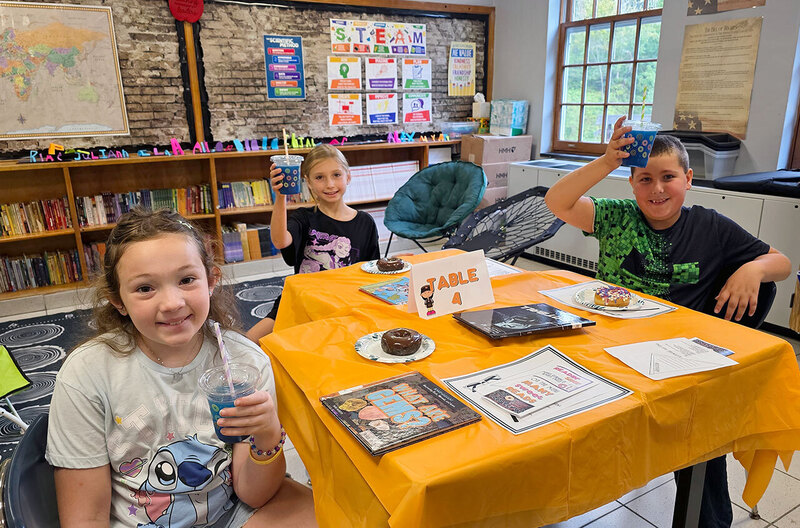 Three students sit at desks with reading materials while enjoying Dunkin donuts and drinks