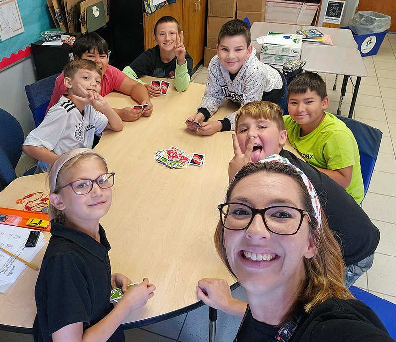 teachers and students sit at table playing card game
