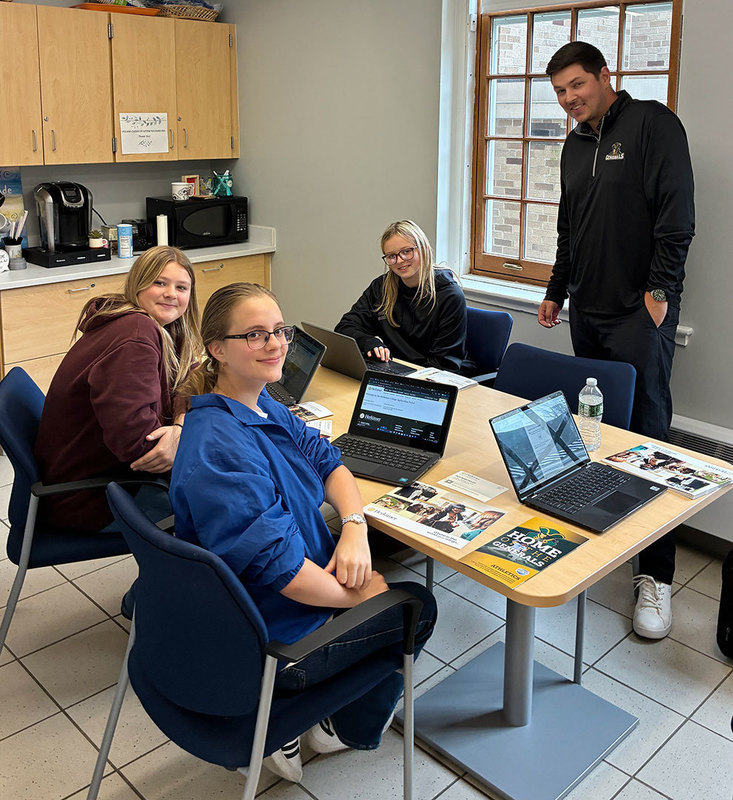 Admissions director stands nearby as three high school students complete online applications to Herkimer College