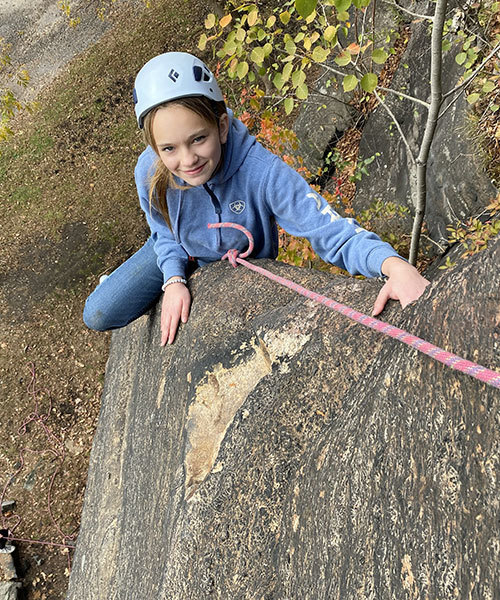 a student wearing a helmut holds onto a rope while climbing a rock ledge