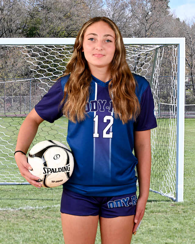Girls soccer player holds soccer ball in front of net