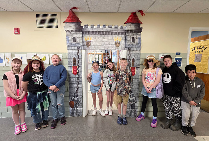 A group of students stand in front of a classroom door that is decorated like the entrance to a castle