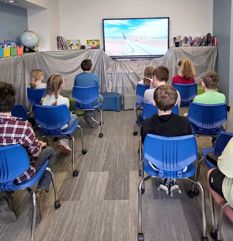 Students sit in rows of chairs set up to simulate the cabin of an airplane
