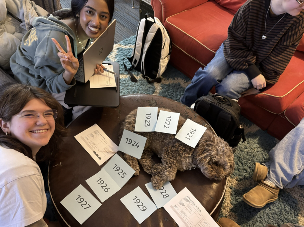 students smiling at camera with notes laying on dog 