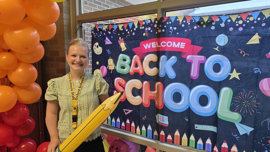Lindsey Vantine, smiling, holding a pencil next to a Back to School banner
