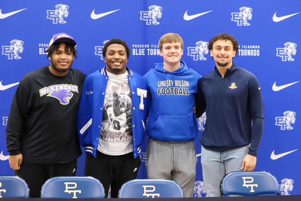 Four athletes stand side by side in front of a banner