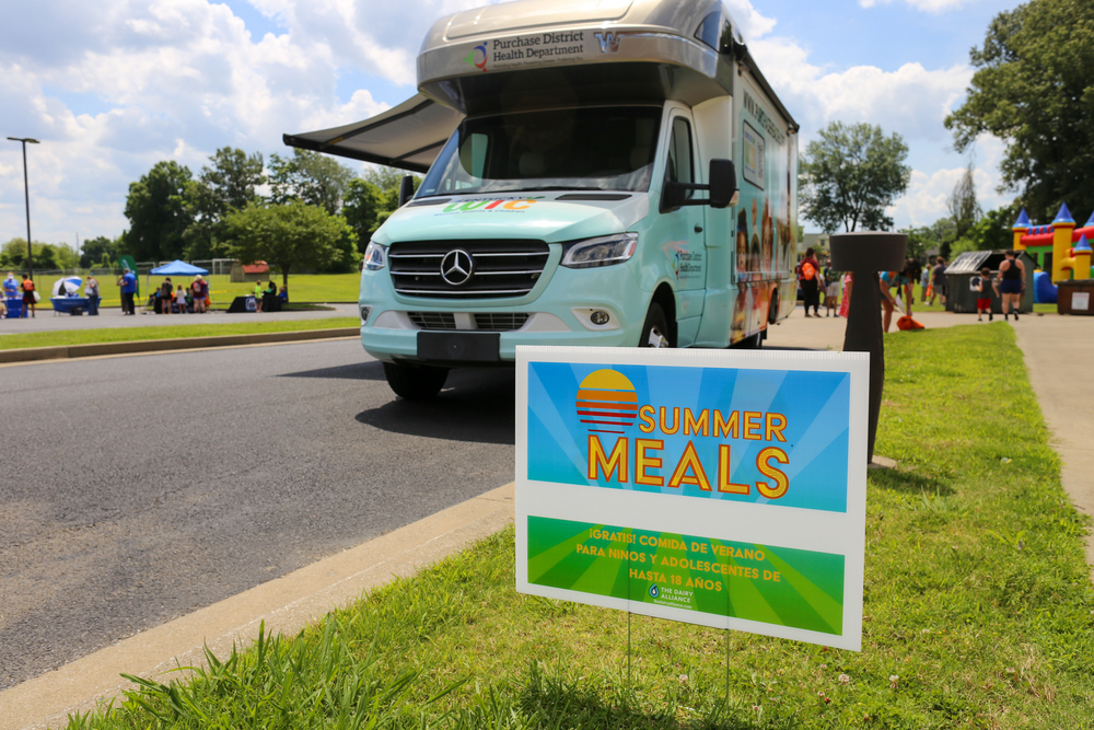 A sign that says "Summer Meals" with a bus in the background