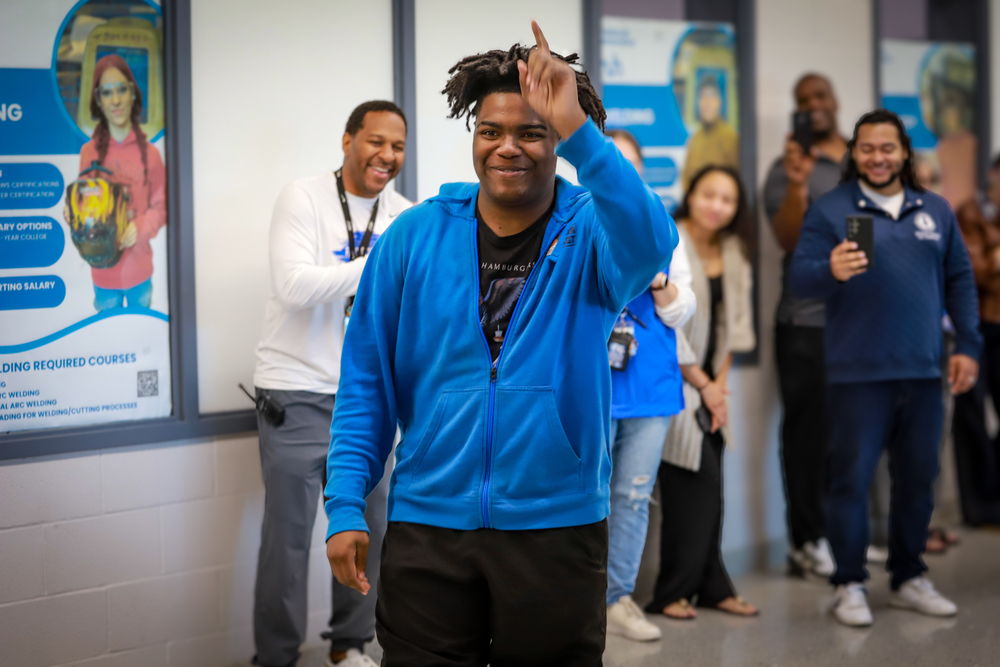 A young man in a blue hoodie points his finger toward the sky