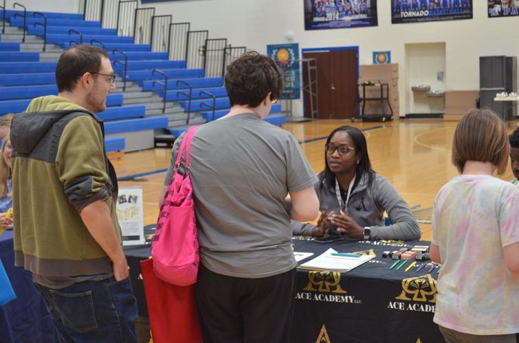 Two teenagers talk to a woman seated at a table in a gym