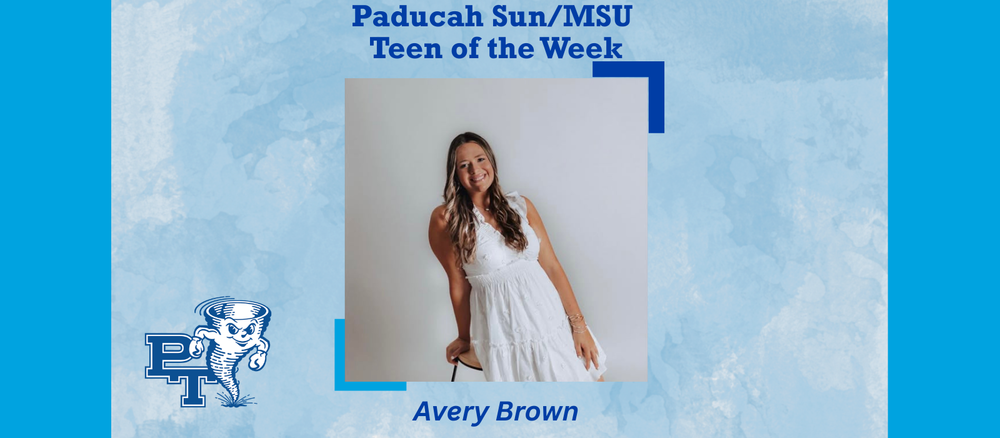 A student in a white dress leans on a stool 