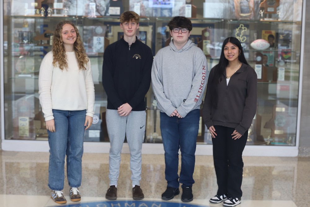 Four high school students stand in front of a trophy case