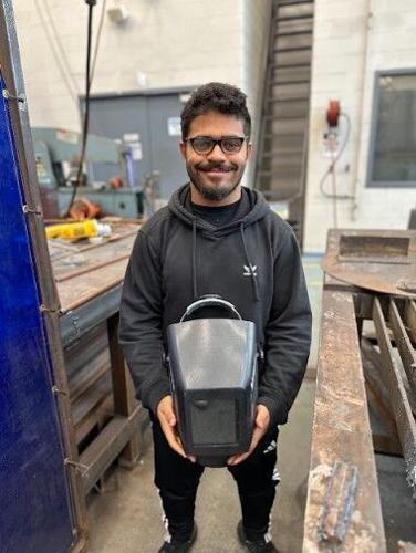 A student stands in a shop, holding a welding mask