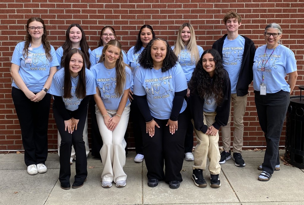 A group of students with teachers pose in front of a brick wall