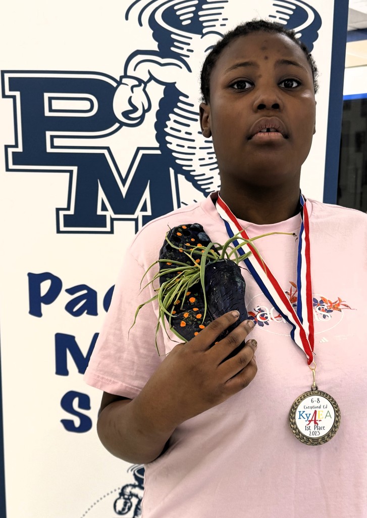 a student holds a 3D sculpture standing next to a banner