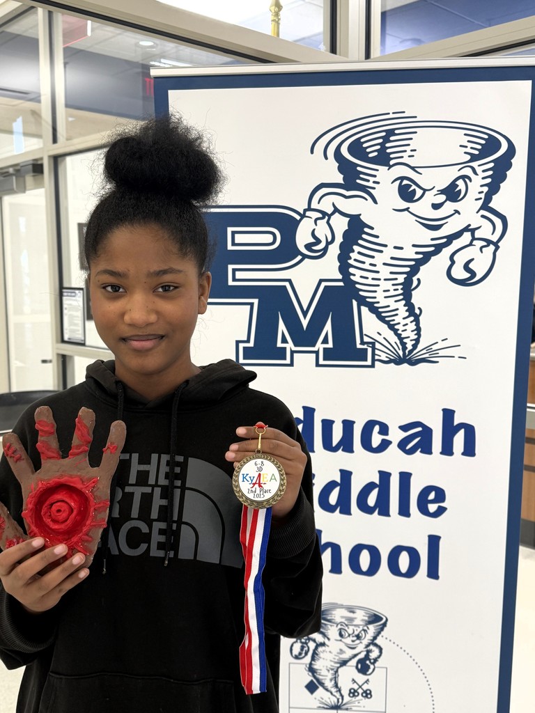 a student holds a 3D sculpture standing next to a banner