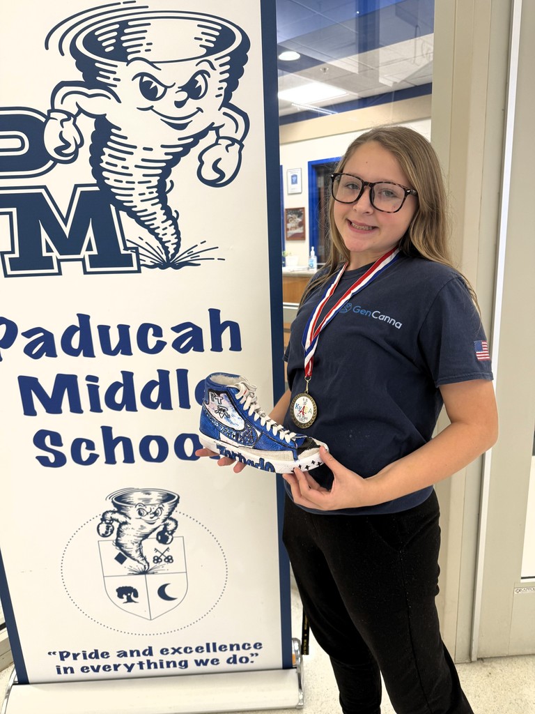 a student holds a 3D sculpture standing next to a banner