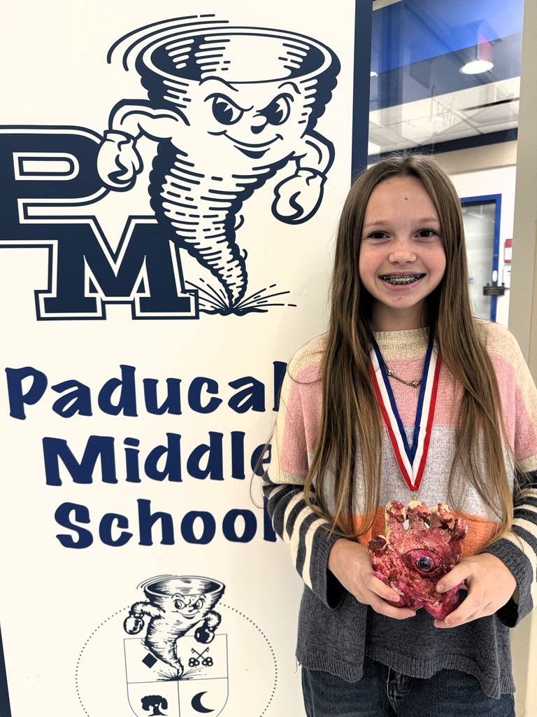 a student holds a 3D sculpture standing next to a banner