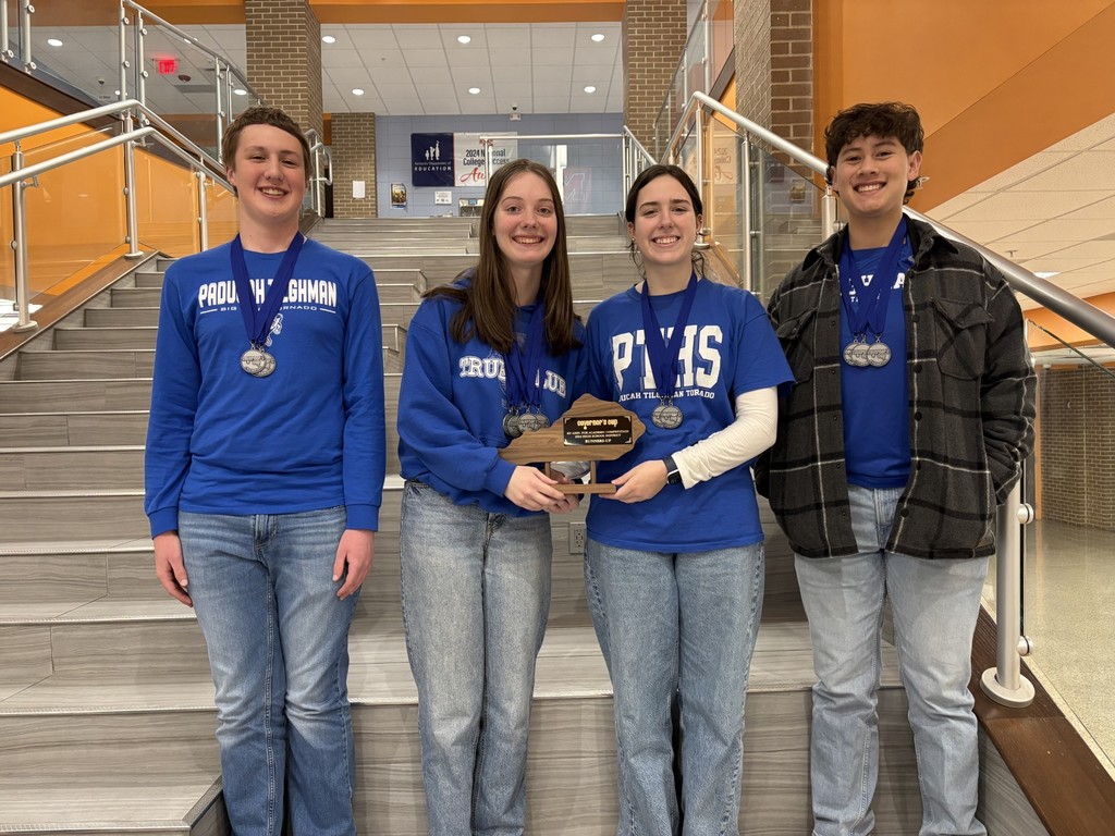 Four individuals wearing blue shirts, one holding a trophy, stand on stairs with handrails. Two are wearing jackets.
