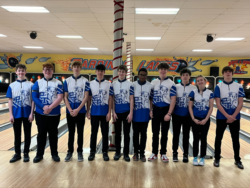 A group of young people in matching blue and white uniforms pose in a bowling alley.