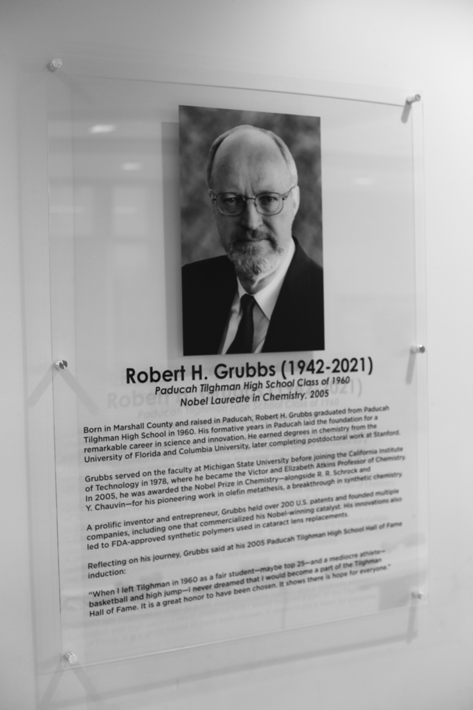 An acrylic plaque displays a photo of Robert H. Grubbs. It reads: "Robert H. Grubbs (1942-2021)" and "Nobel Laureate in Chemistry."