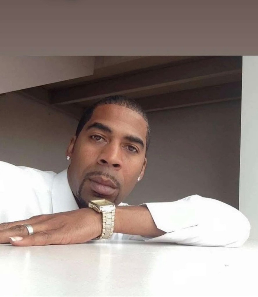A man with a beard, wearing a white shirt, rests his elbows on a table. 