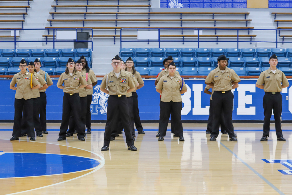 A group of uniformed individuals standing on a basketball court with a blue and white floor.