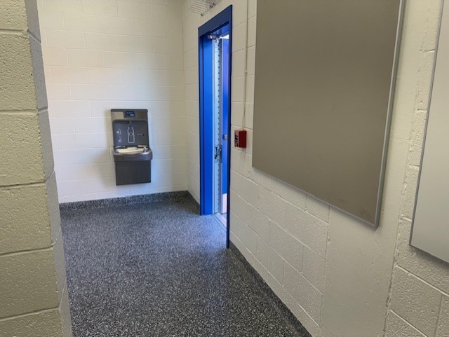 Empty room with gray walls, gray floor, and a blue door. A gray board is on the right wall.