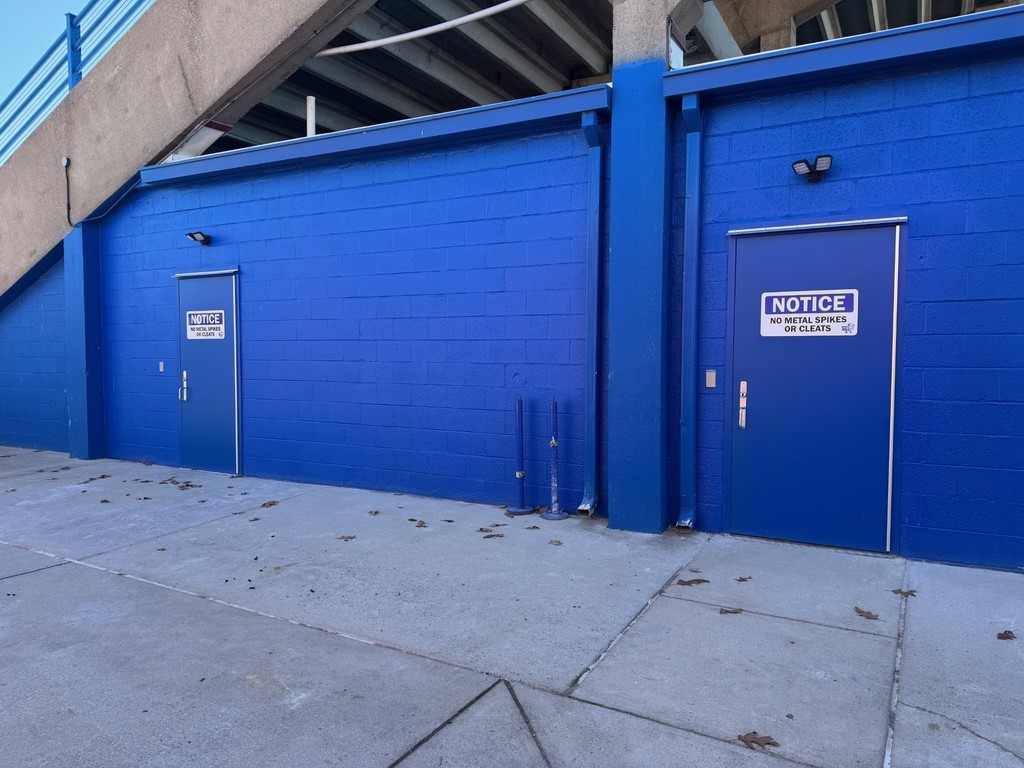 Two blue doors with signs on a building. Stairs and a walkway are in the background.