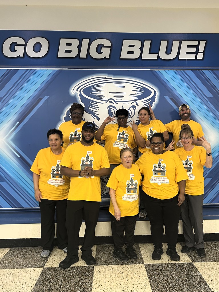 A group of people in yellow shirts pose for a photo in front of a banner.