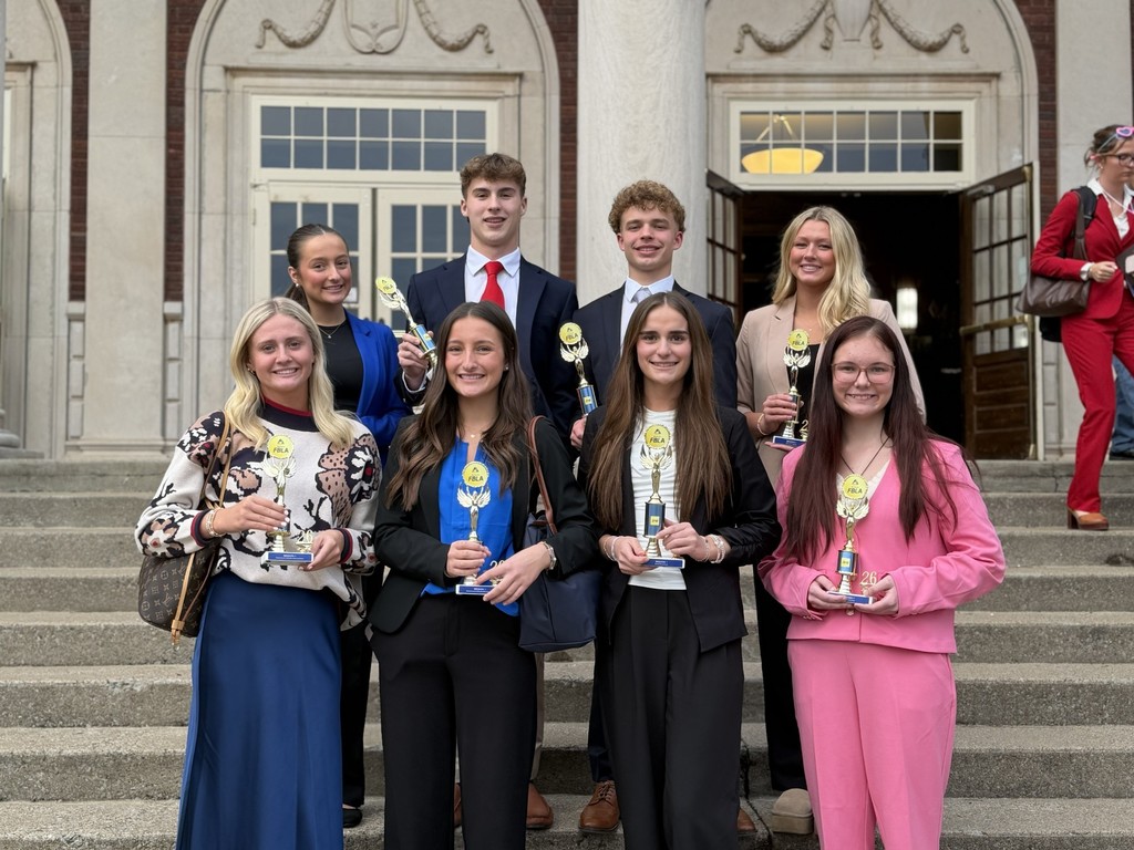 Group of students with awards on the steps of a building with columns and arched doorway.