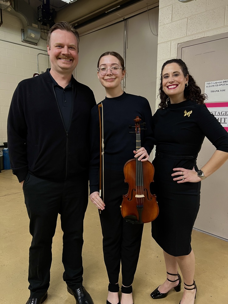 Young string player flanked by her parents.
