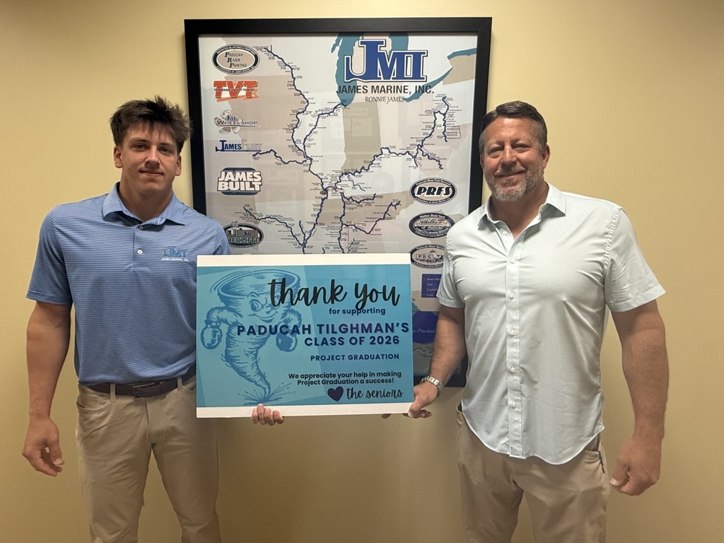 Two men standing in front of a map, one holding a sign thanking the Padmcan Tilohmann Class of 2020.
