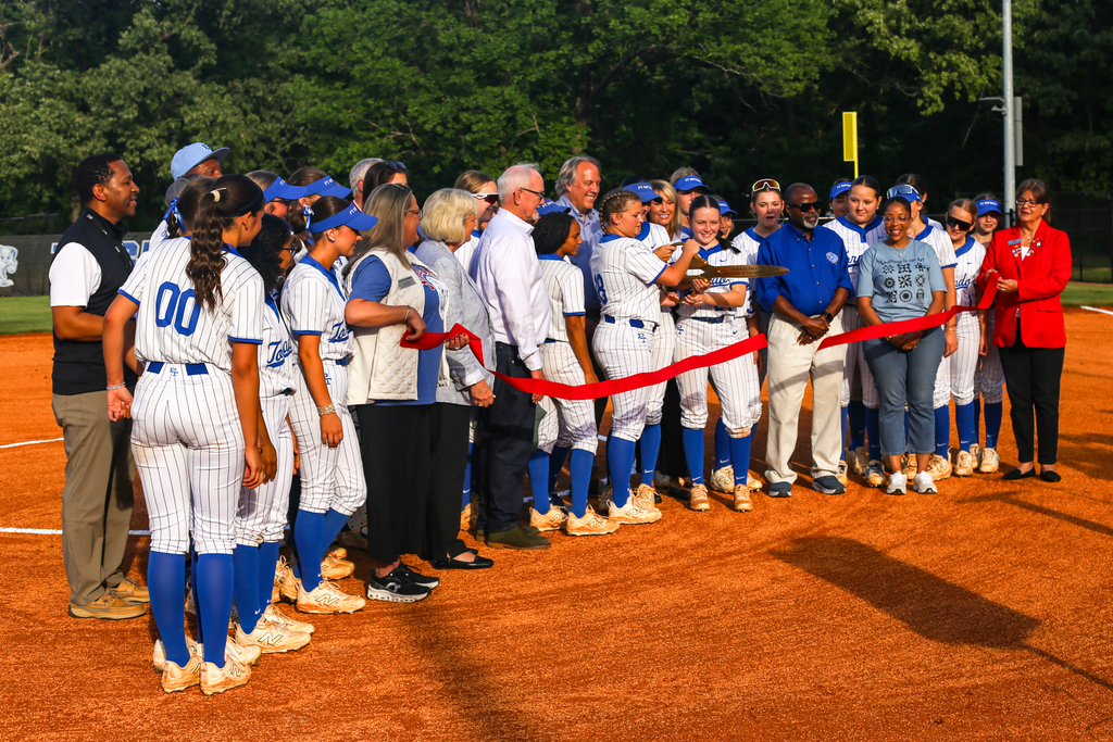A group of people, wearing blue and white uniforms, stand in a line with a red ribbon.