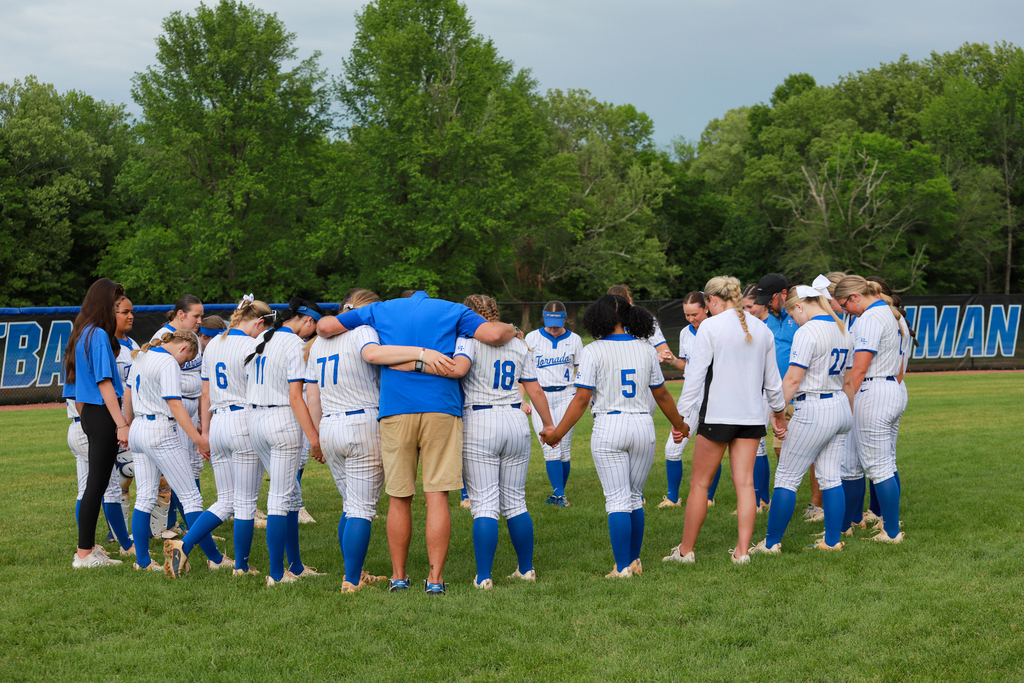 A team of women in blue and white uniforms stand in a circle with a man in a blue shirt.
